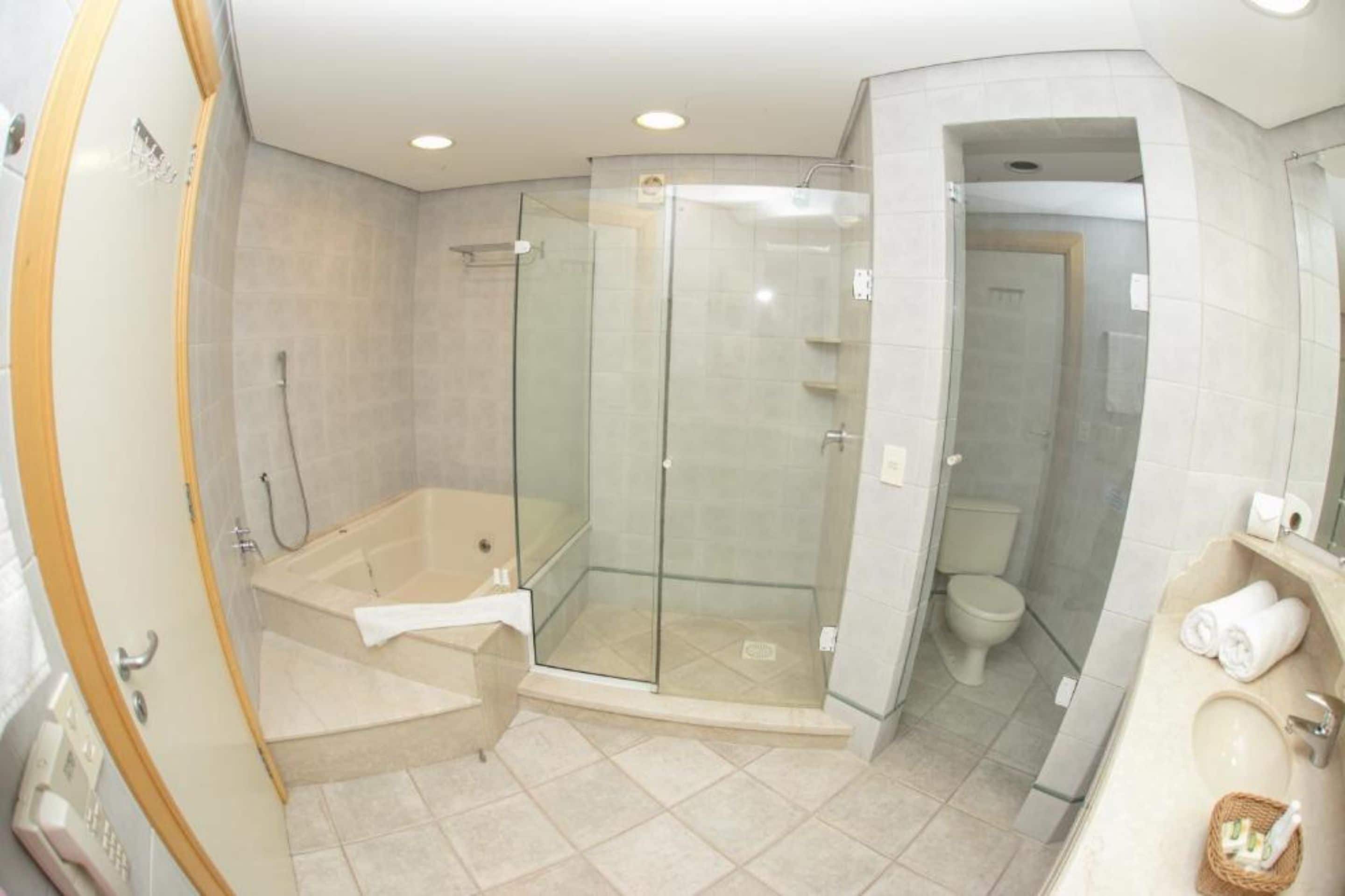 Un baño moderno con ducha envuelta en vidrio, una bañera independiente y un área separada para el inodoro.