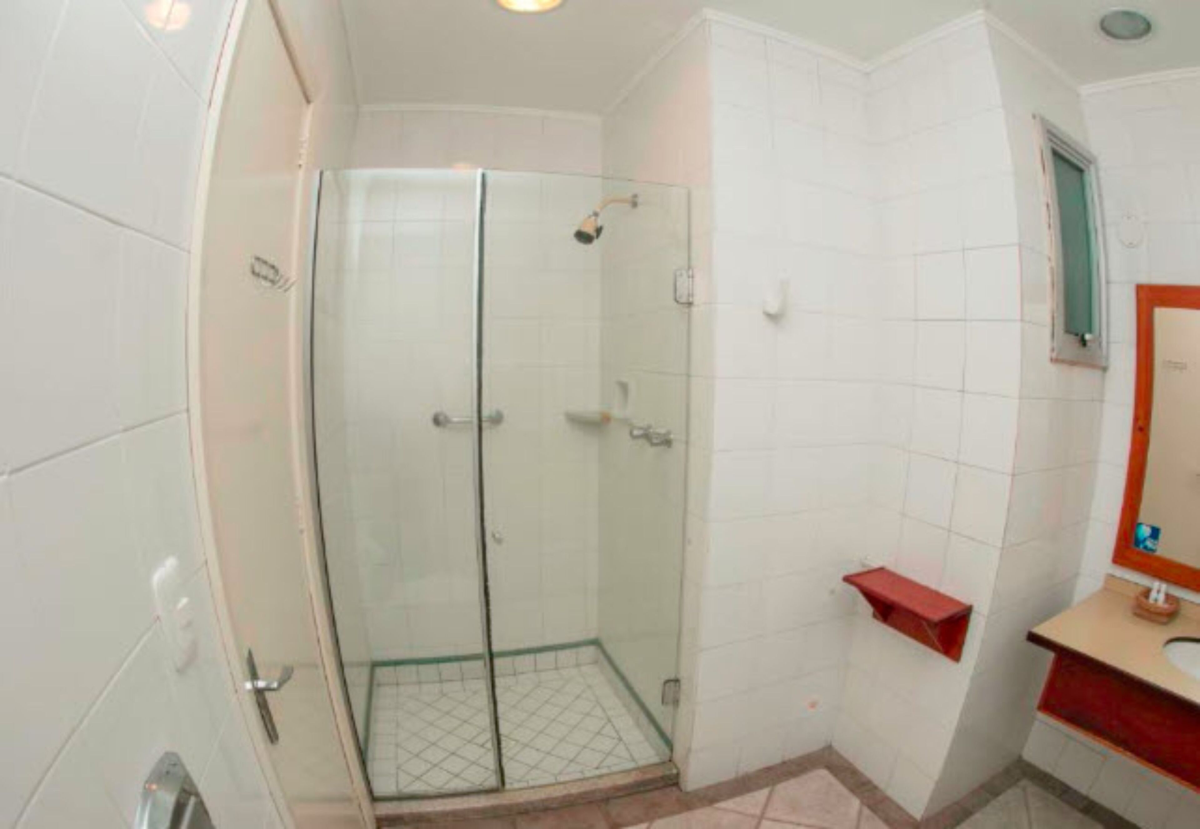 Une salle de bain avec des murs recouverts de carreaux blancs, une douche en verre, un porte-serviettes rouge et un miroir avec un cadre en bois.