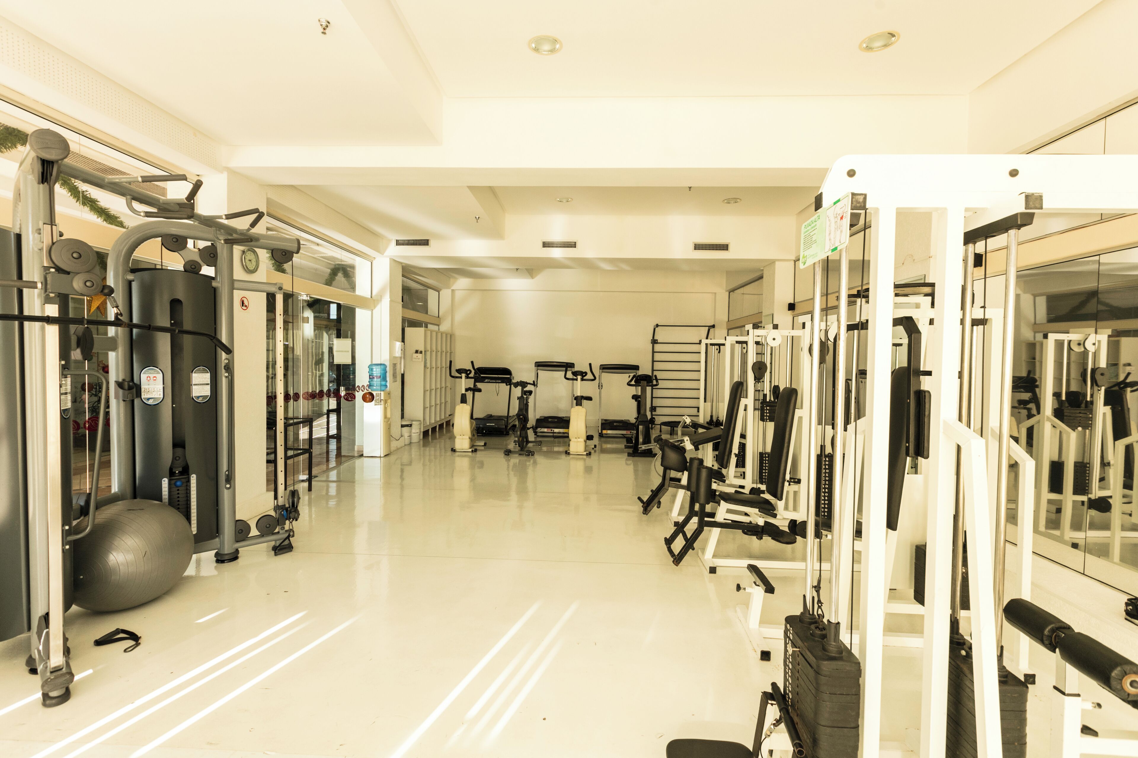 Un gimnasio con diversas máquinas de ejercicio, una pelota grande para hacer ejercicio y un espejo grande en la pared.