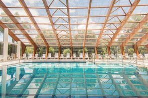 En indendørs swimmingpool med kig til himlen gennem en trætagkonstruktion.