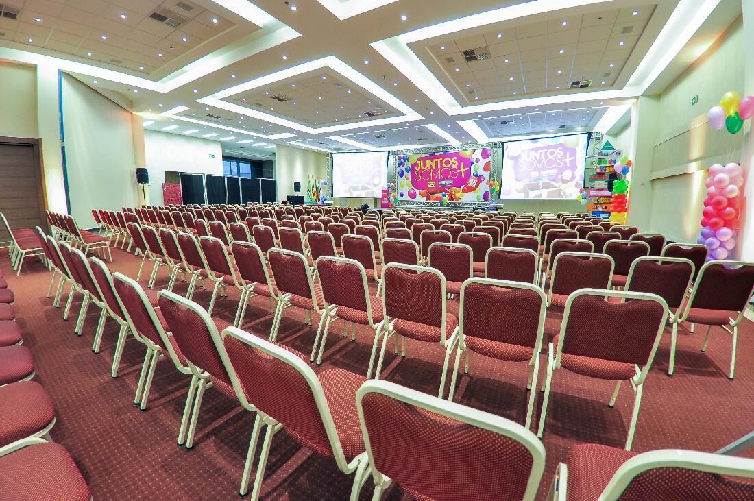 A conference room with rows of red chairs, a stage with a colorful backdrop, and a speaker system.