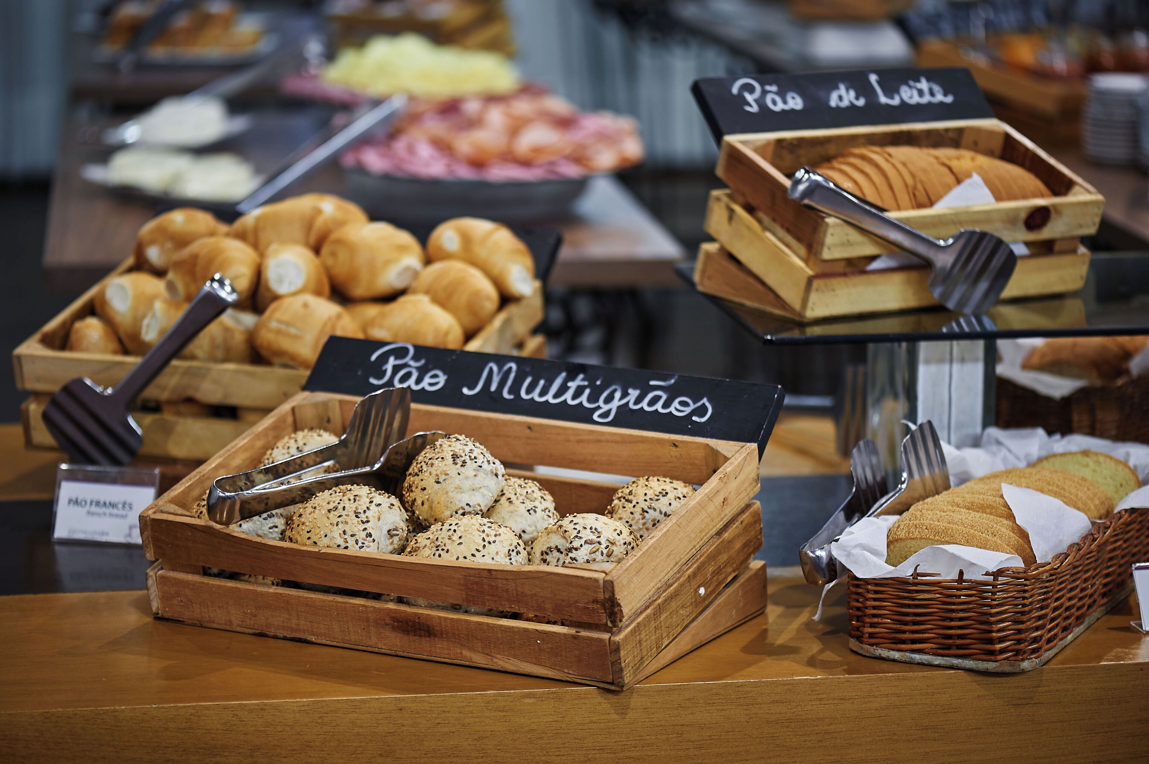 A bakery display with various types of bread and pastries, including a sign for 'Pão de Leite'.