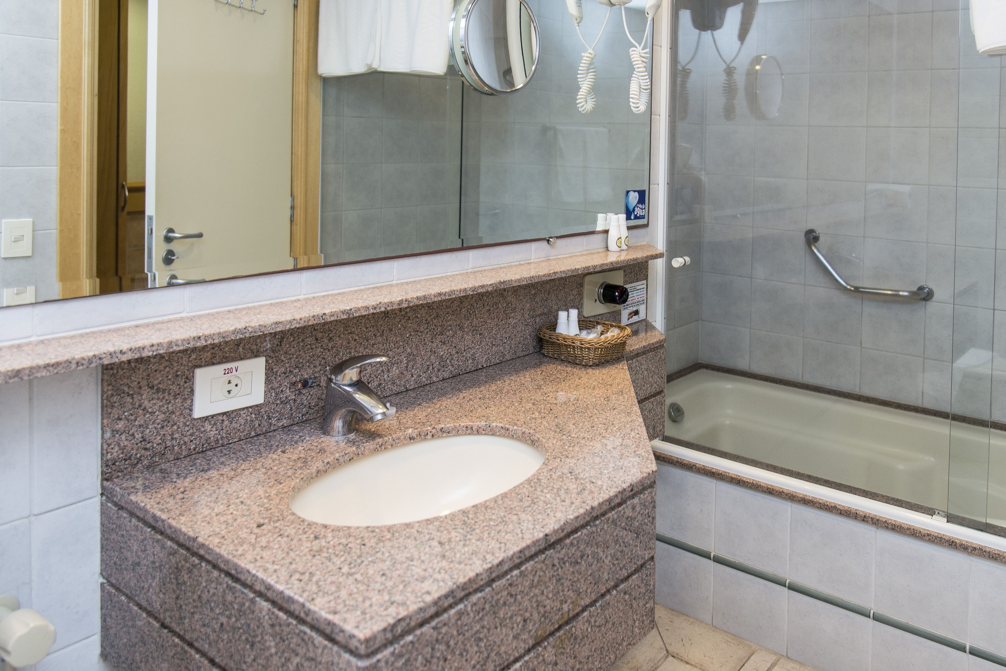 A bathroom with a granite countertop sink, a mirror, a towel rack, and a glass-enclosed shower.