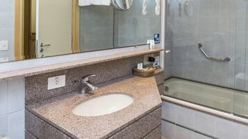 A bathroom with a granite countertop sink, a mirror, a towel rack, and a glass-enclosed shower.