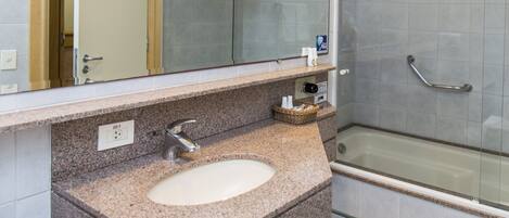 A bathroom with a granite countertop sink, a mirror, a towel rack, and a glass-enclosed shower.