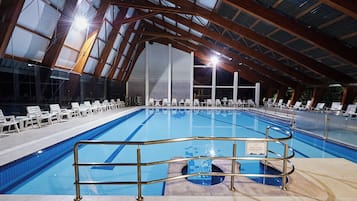 Une piscine intérieure dotée d’un haut plafond et de verrières, entourée de chaises longues.