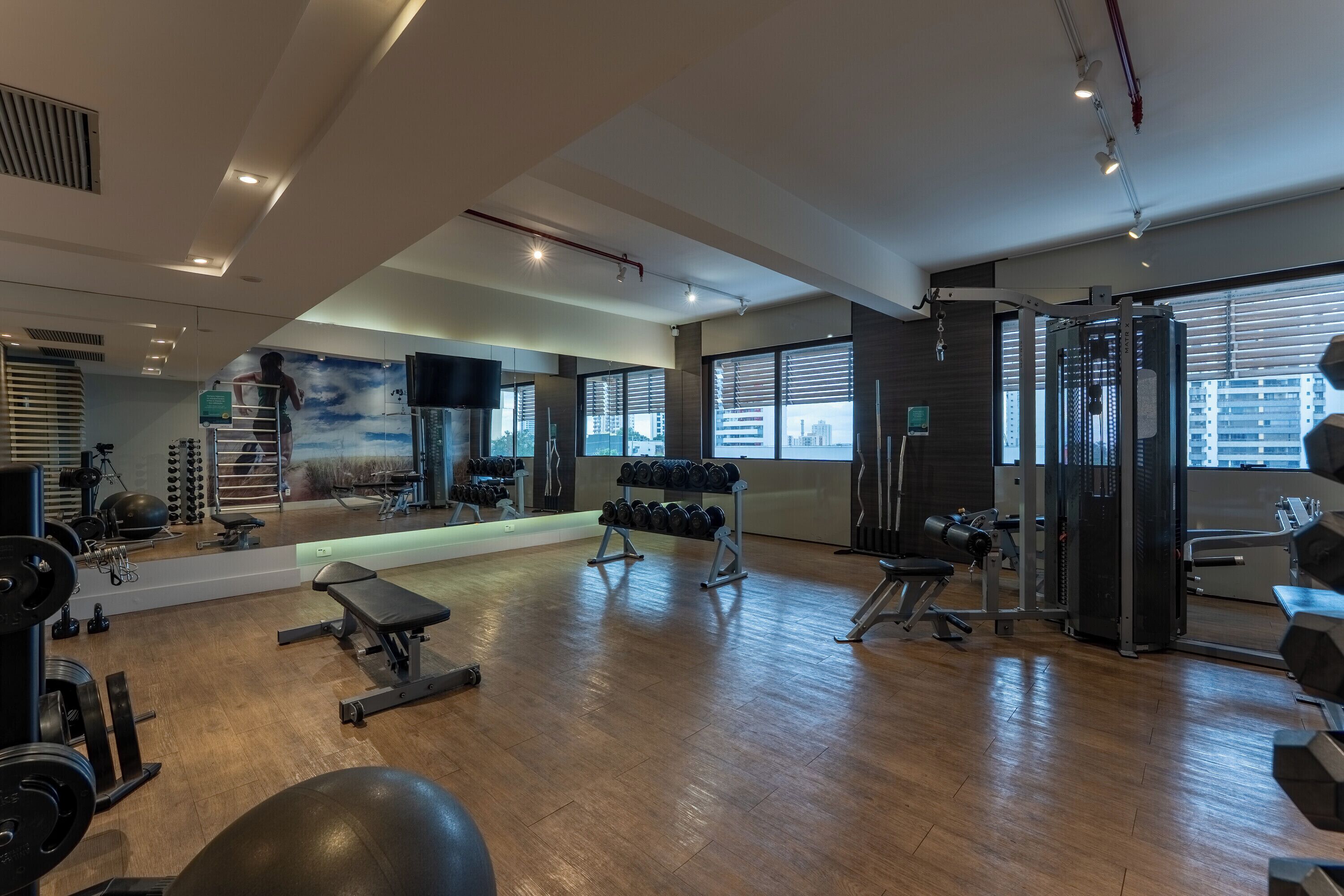 A gym with various exercise equipment, a mirror wall, and large windows.