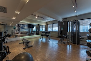 Un gimnasio con equipo de ejercicio diverso, un muro de espejos y ventanas grandes.