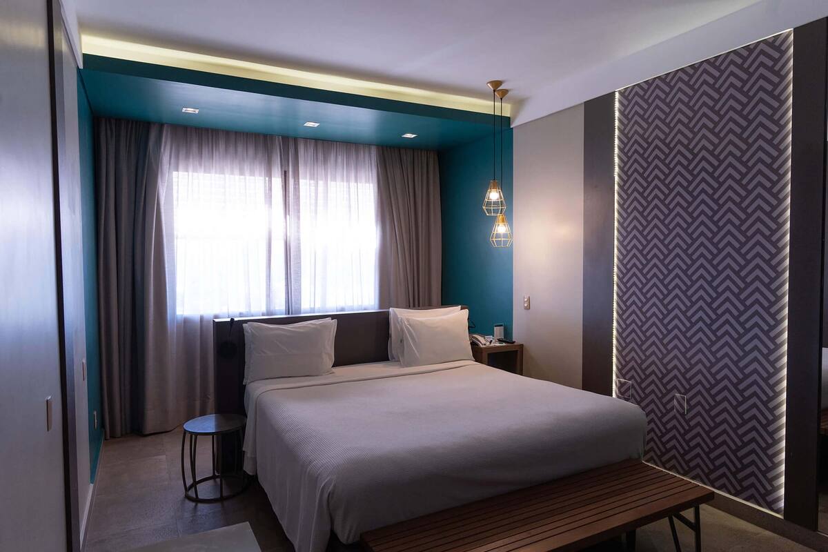Une chambre d’hôtel moderne avec un grand lit, une table de chevet, une petite table ronde et un banc.