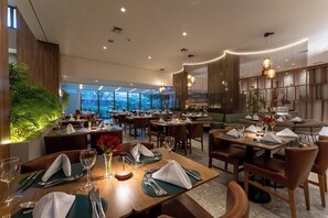 A restaurant with multiple dining tables, chairs, and a view of the cityscape through large windows. - Hotel Deville Prime Cuiabá (Cuiabá)