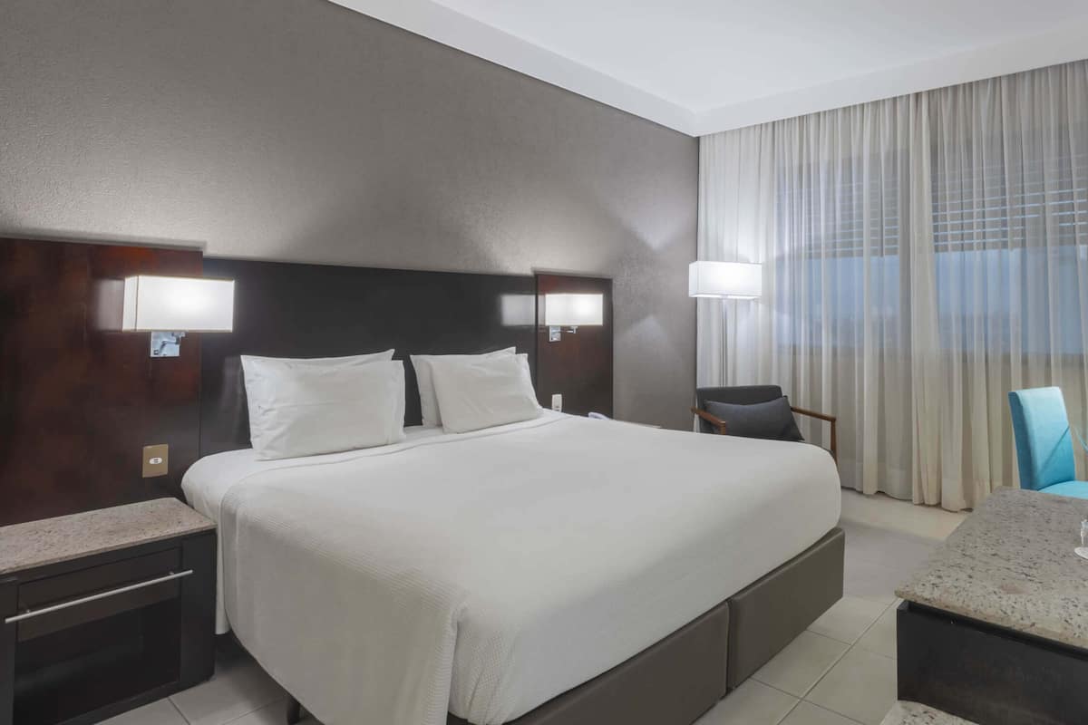 Une chambre d’hôtel avec un grand lit, deux tables de chevet, un bureau avec une chaise et une fenêtre avec des rideaux.