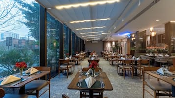 A restaurant with multiple dining tables and chairs, large windows, and a modern ceiling design.
