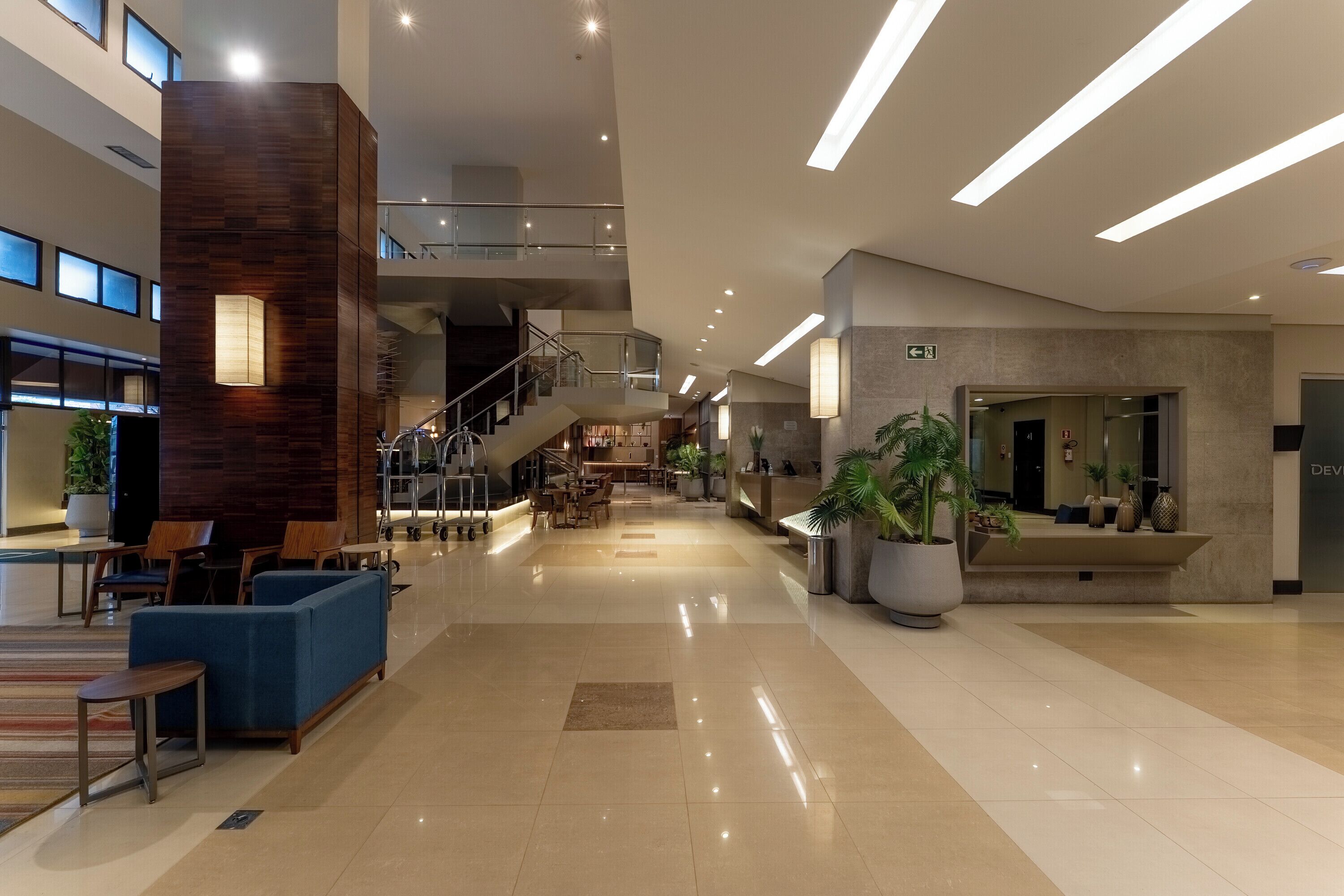 Um hall amplo com balcão de recepção, área de estar e escada que leva aos andares superiores.