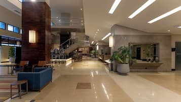 Um hall amplo com balcão de recepção, área de estar e escada que leva aos andares superiores.