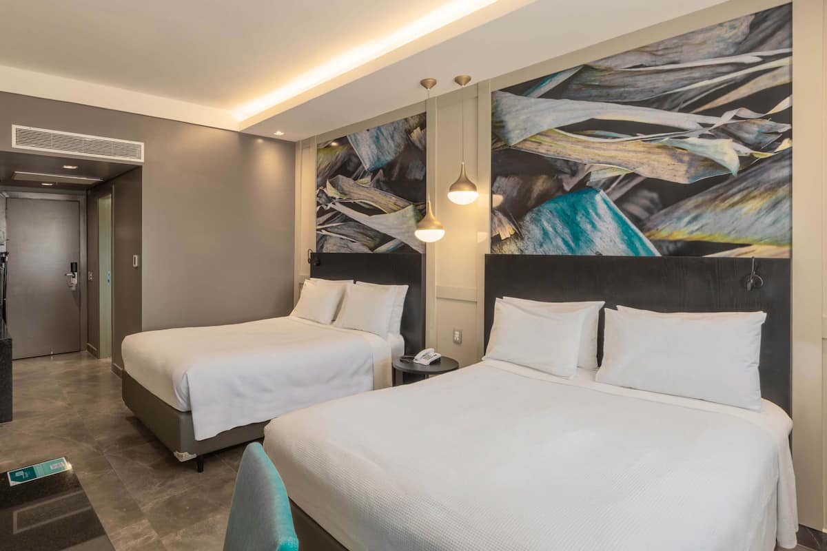 Une chambre d’hôtel avec deux lits, une grande peinture abstraite au mur et un luminaire moderne.