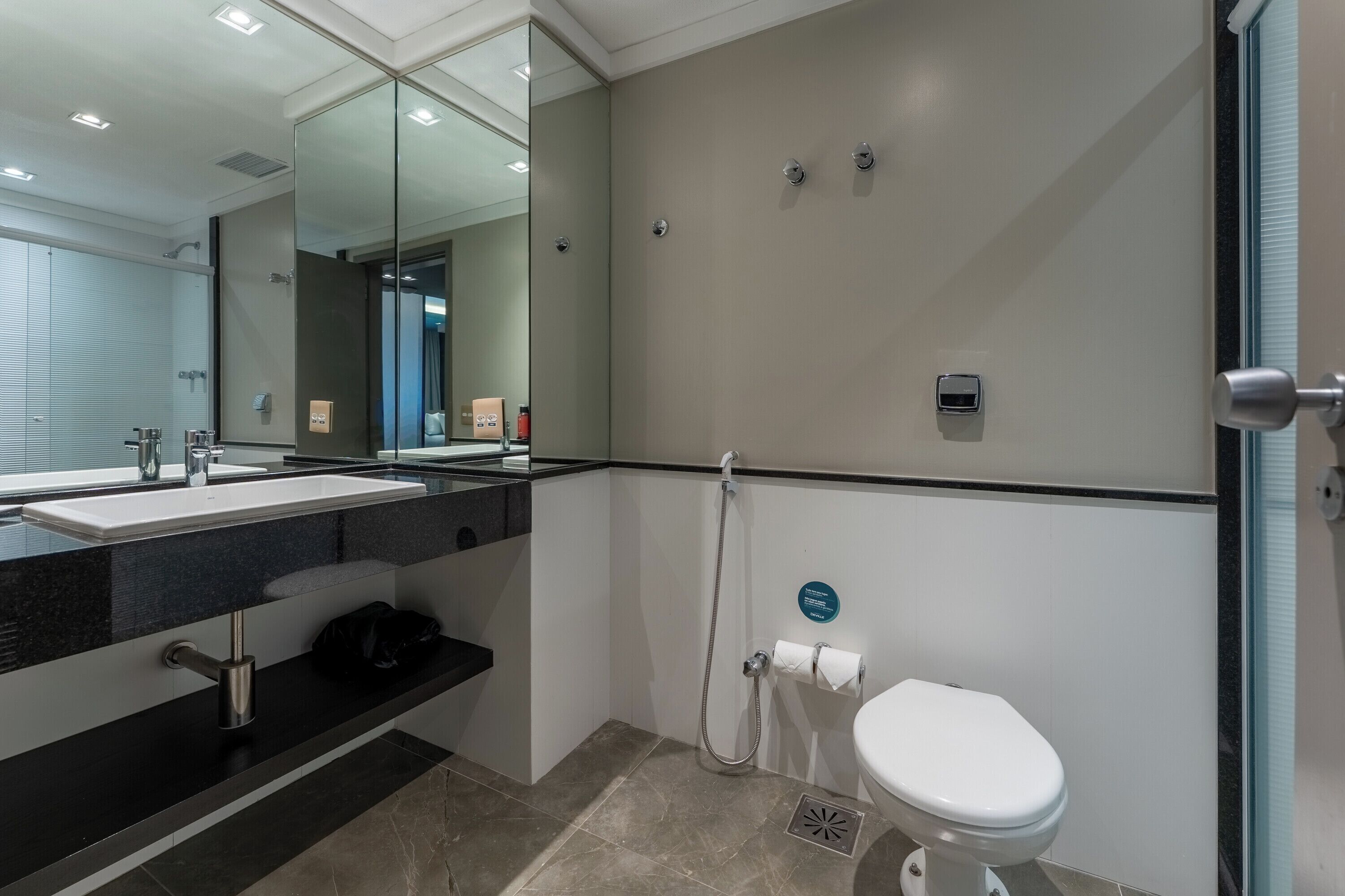 A modern bathroom with a large mirror, a sink, a toilet, and a shower area.