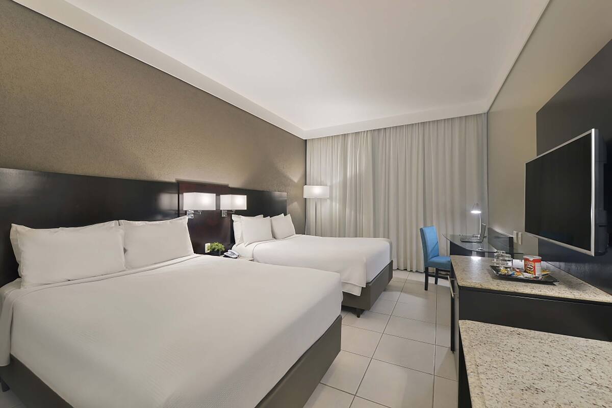 Une chambre d’hôtel avec deux lits, un bureau doté d’un téléviseur à écran plat, une chaise et une table à manger avec un plateau de collations.