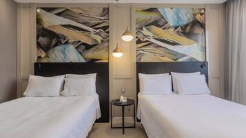 A hotel room with two beds, a small table with a phone, and a wall with abstract art.