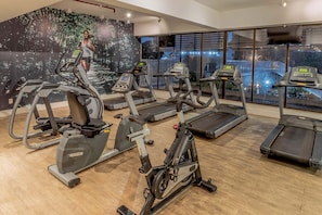A gym with treadmills, stationary bikes, and a mural of a runner.