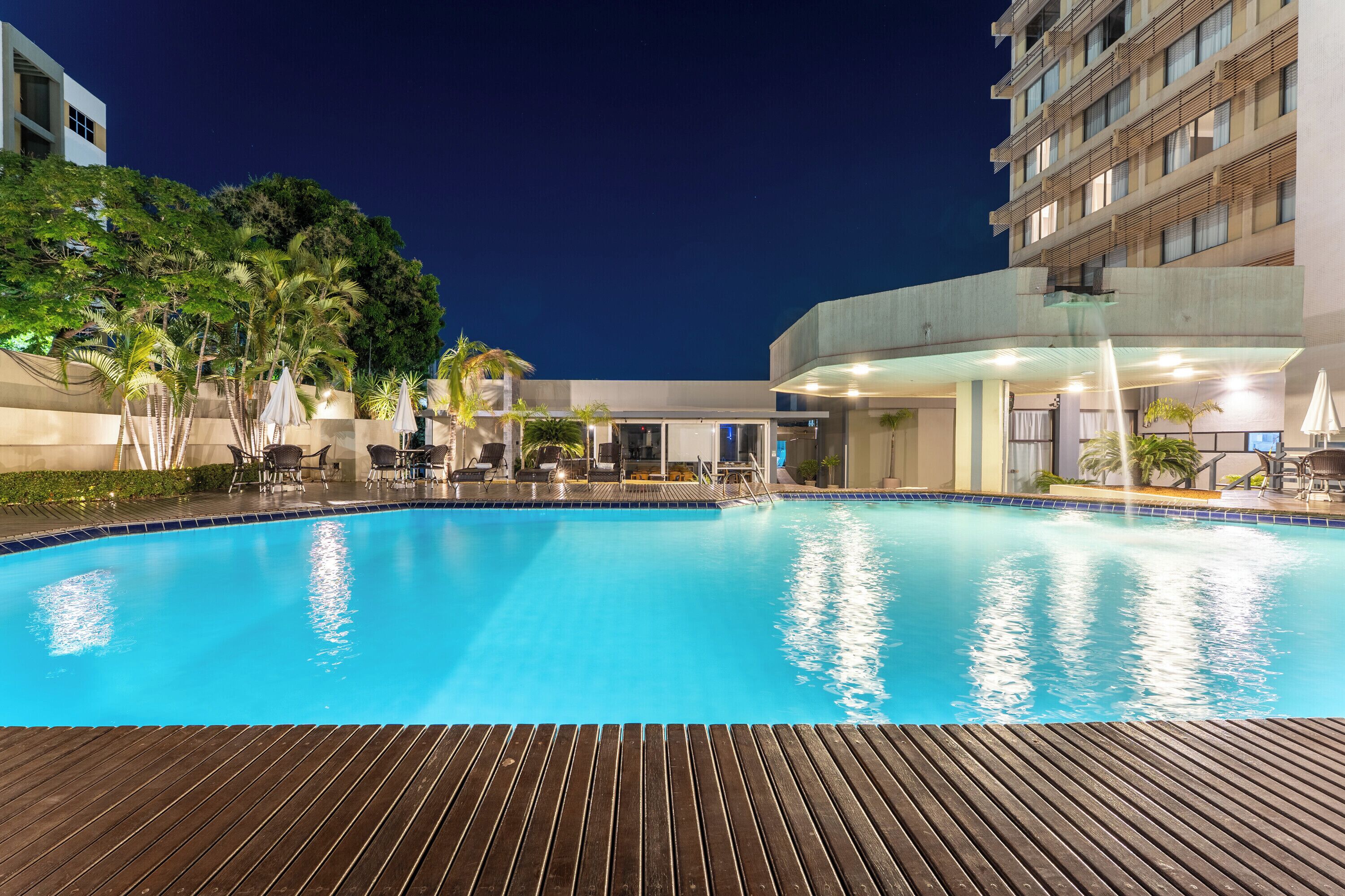 A swimming pool with a wooden deck in the foreground, surrounded by lounge chairs and umbrellas.