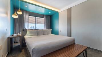 Habitació d'hotel moderna amb un llit gran, una banca de fusta, un escriptori amb un telèfon i vistes a la ciutat.