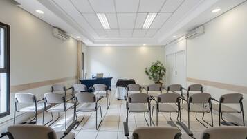 Uma sala de conferências com fileiras de cadeiras, uma mesa e um vaso de plantas.