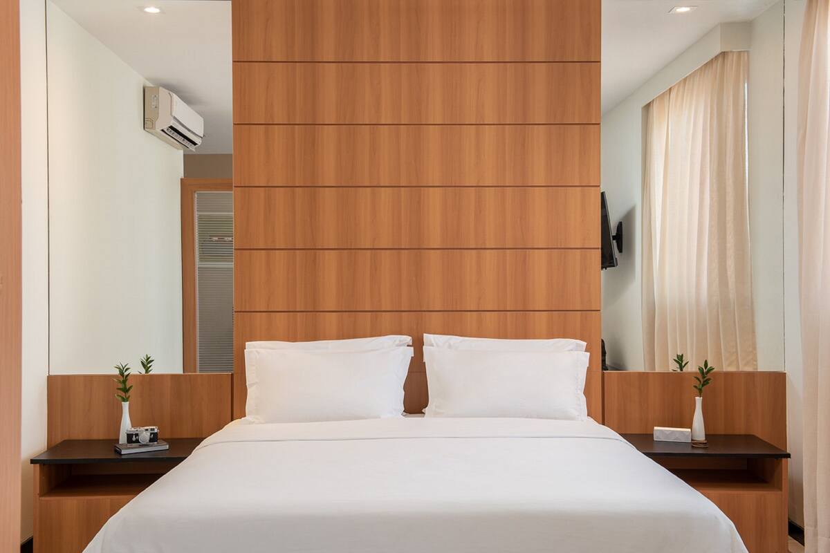 Une chambre d’hôtel avec un grand lit, une tête de lit en bois, des tables de chevet ornées de vases et un téléviseur fixé au mur.