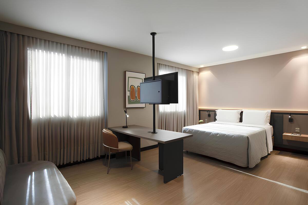 Une chambre d’hôtel avec un lit, un bureau et une chaise, une télévision et des rideaux.