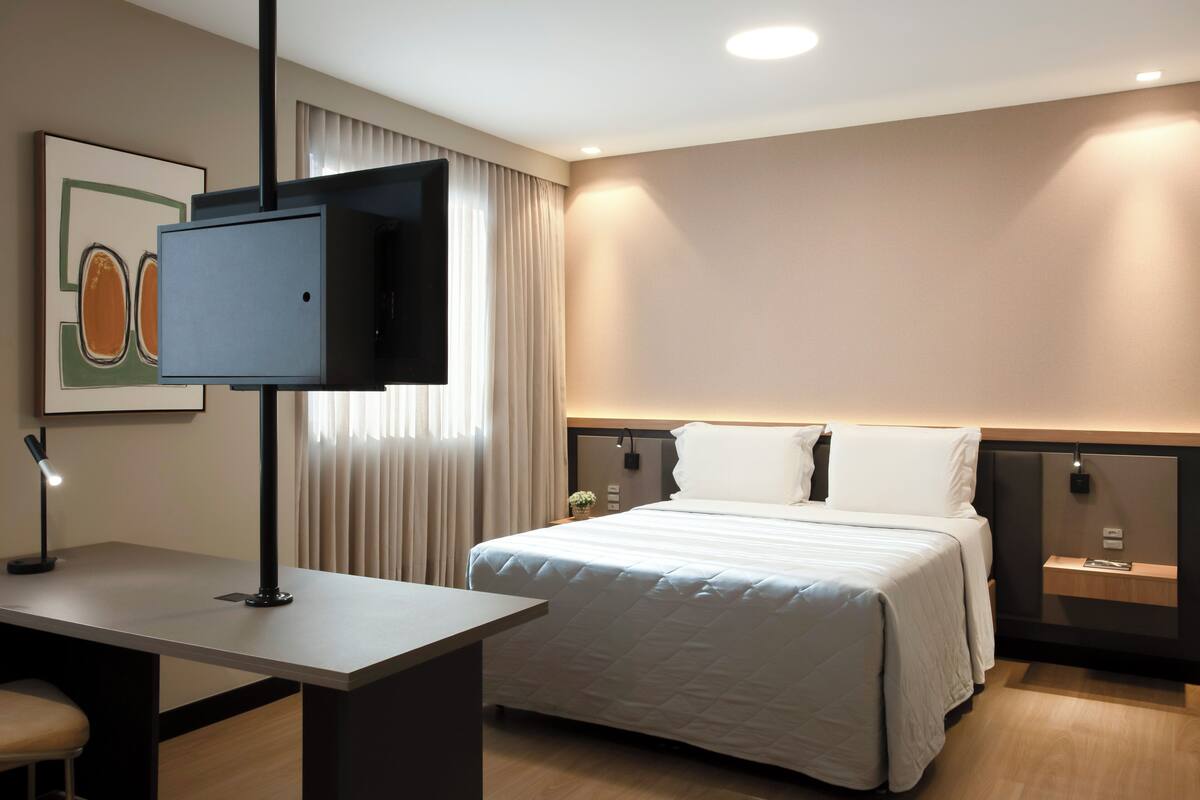 Une chambre d’hôtel moderne équipée d’un lit, d’un bureau, d’une télévision à écran plat et d’une table de chevet.