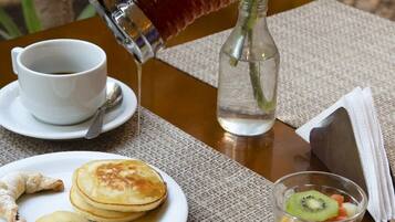A breakfast setting with pancakes, a muffin, a cup of coffee, a glass of juice, and a vase with red flowers.
