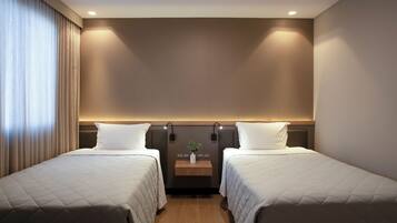 A hotel room with two beds, a bedside table with a plant, and a wall-mounted light fixture.
