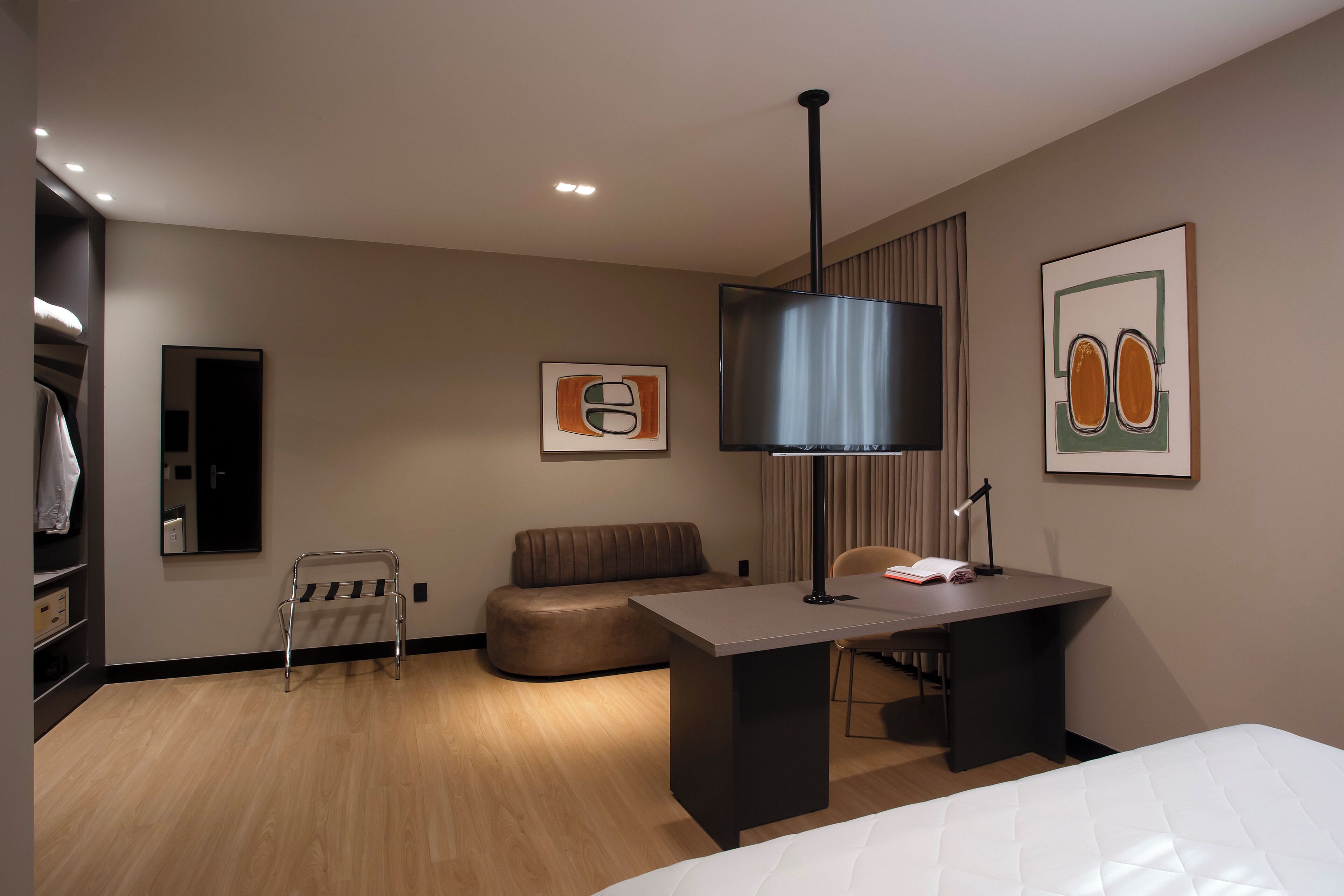 Una habitación de hotel moderna con cama, escritorio, silla, banco y armario.