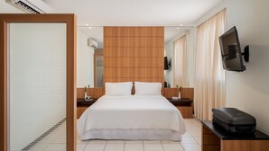 Een moderne hotelkamer met een groot bed, een houten hoofdeinde, een flatscreen-tv aan de muur, een nachtkastje met een lamp en een koffer op een bijzettafeltje.