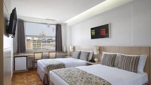 Habitació d'hotel amb dos llits, un escriptori, un televisor i una finestra que dona a la vista de la ciutat.