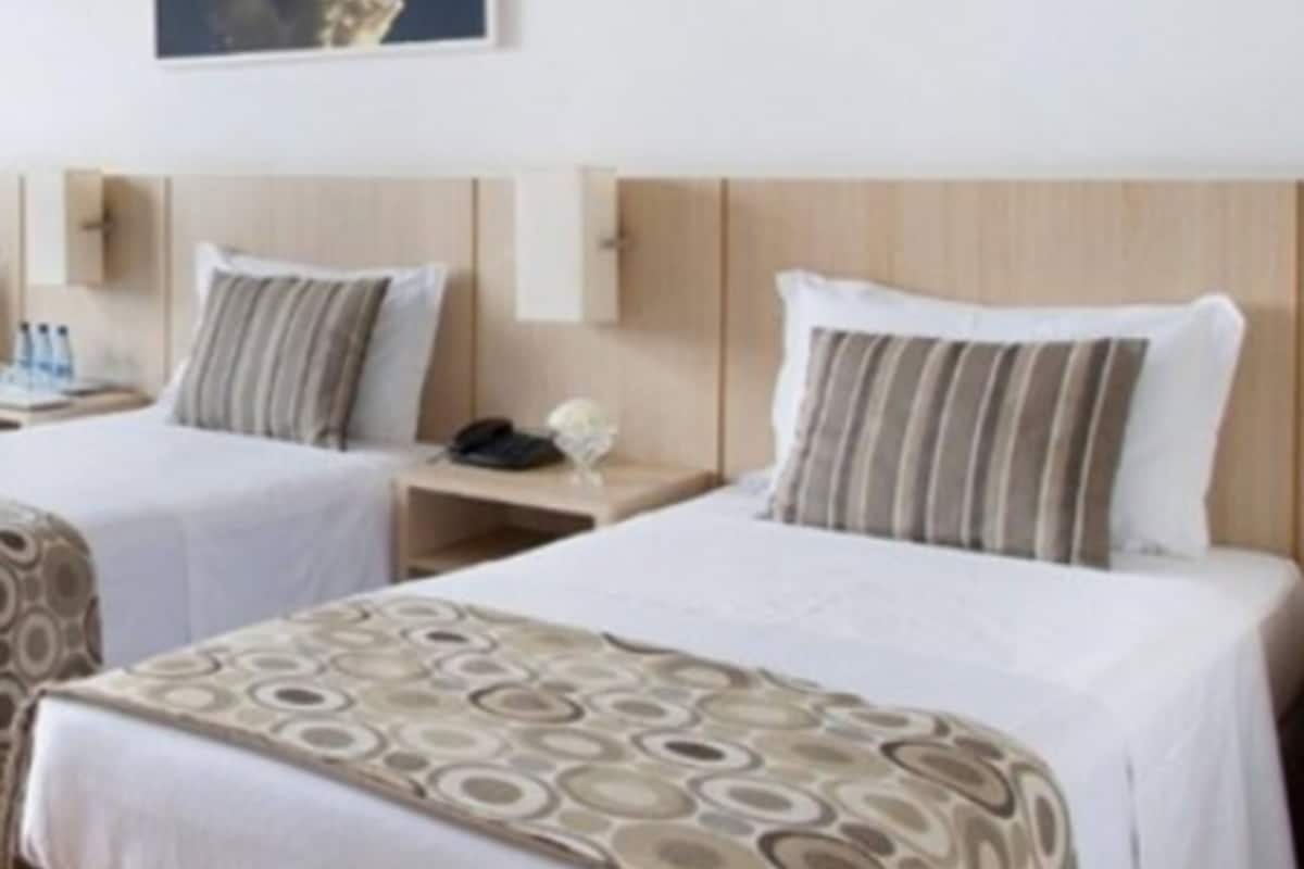 A hotel room with two beds, each with a headboard and bedside tables. There is a framed picture on the wall above the beds.