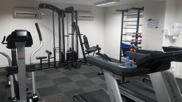 Uma academia com diversos equipamentos de exercícios, incluindo esteira, aparelhos de musculação e um banco.