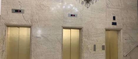 A marble-floored lobby with three gold elevators and a trash can.