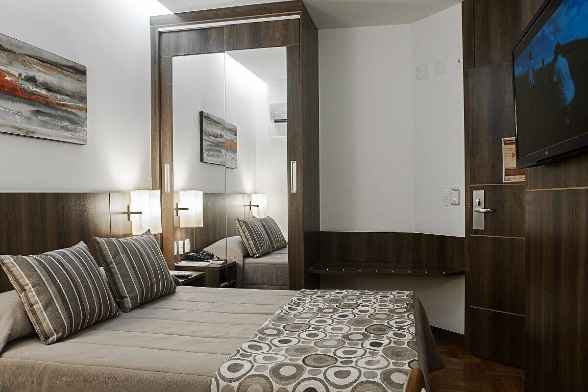 A hotel room with a bed, bedside tables, a mirror, a TV, and a wardrobe.