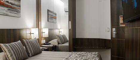 Habitación de hotel con cama, mesitas de noche, espejo, televisor y armario.