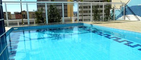 A swimming pool with a tiled edge, surrounded by a white fence and palm trees.