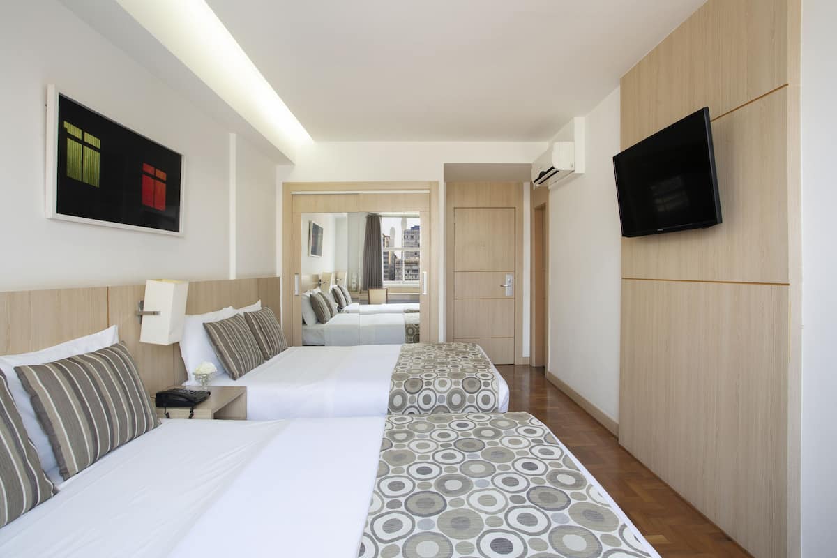 A hotel room with two beds, a TV, and a view of the city.
