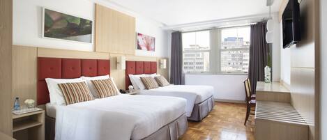 A hotel room with two beds, a TV, a window with a view of buildings, and a wooden floor.