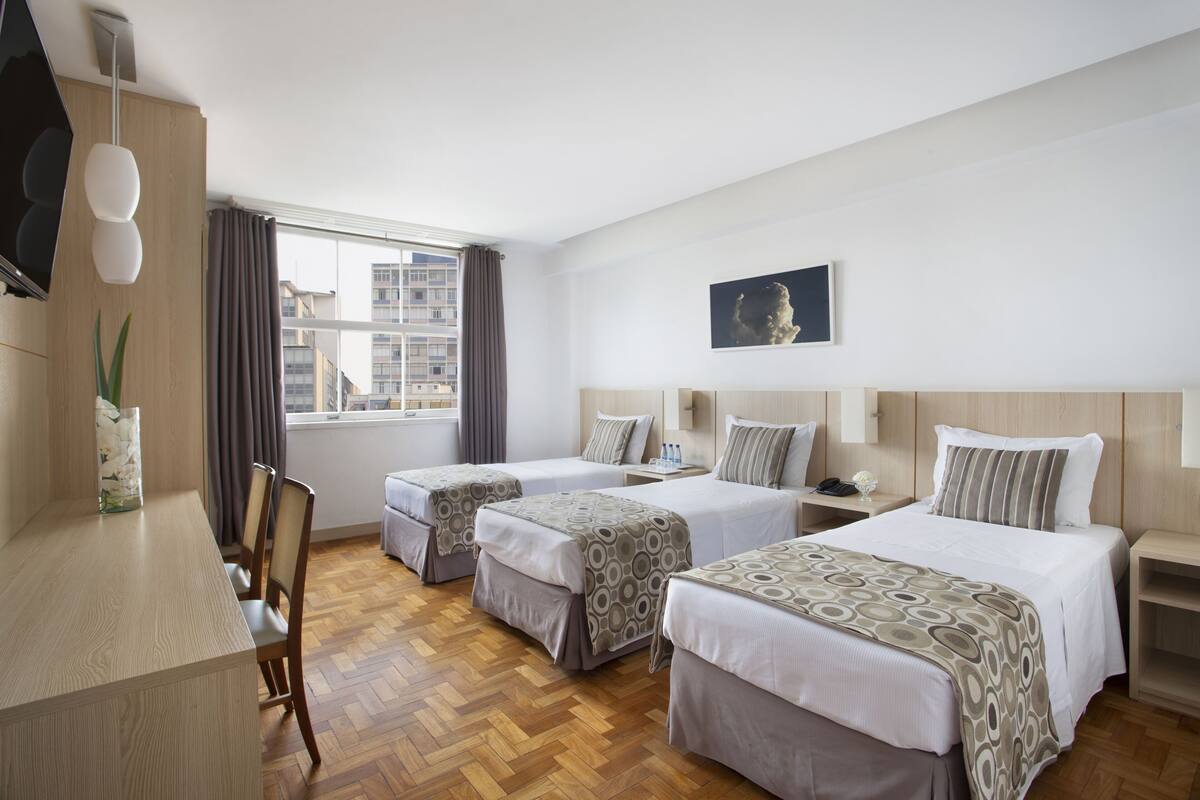 A hotel room with two beds, a desk, and a TV.