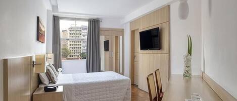 Una habitación de hotel con una cama, un escritorio, una silla, un televisor y una ventana con cortinas.