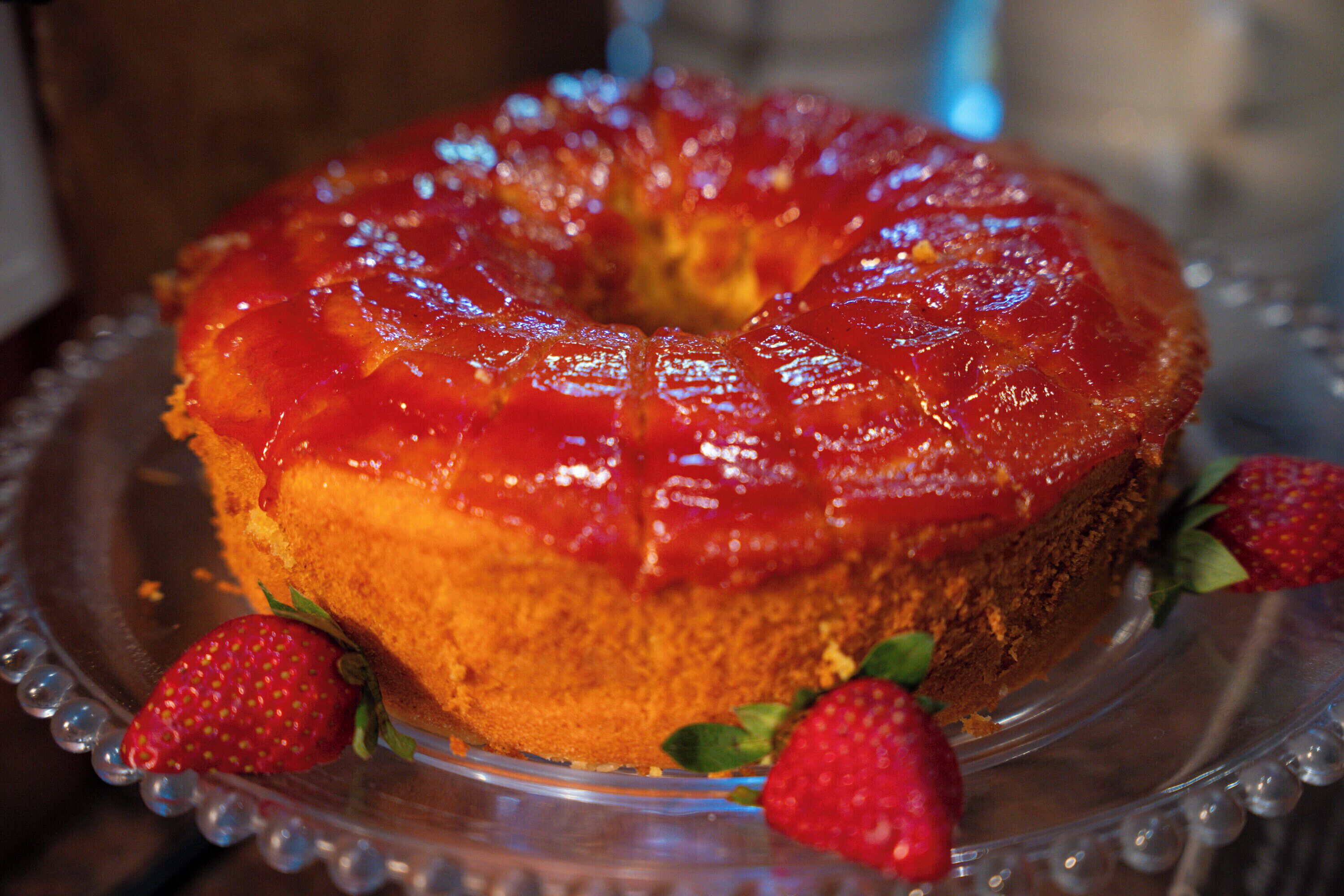 Un pastel Bundt con un glaseado brillante y fresas sobre un plato de vidrio transparente.