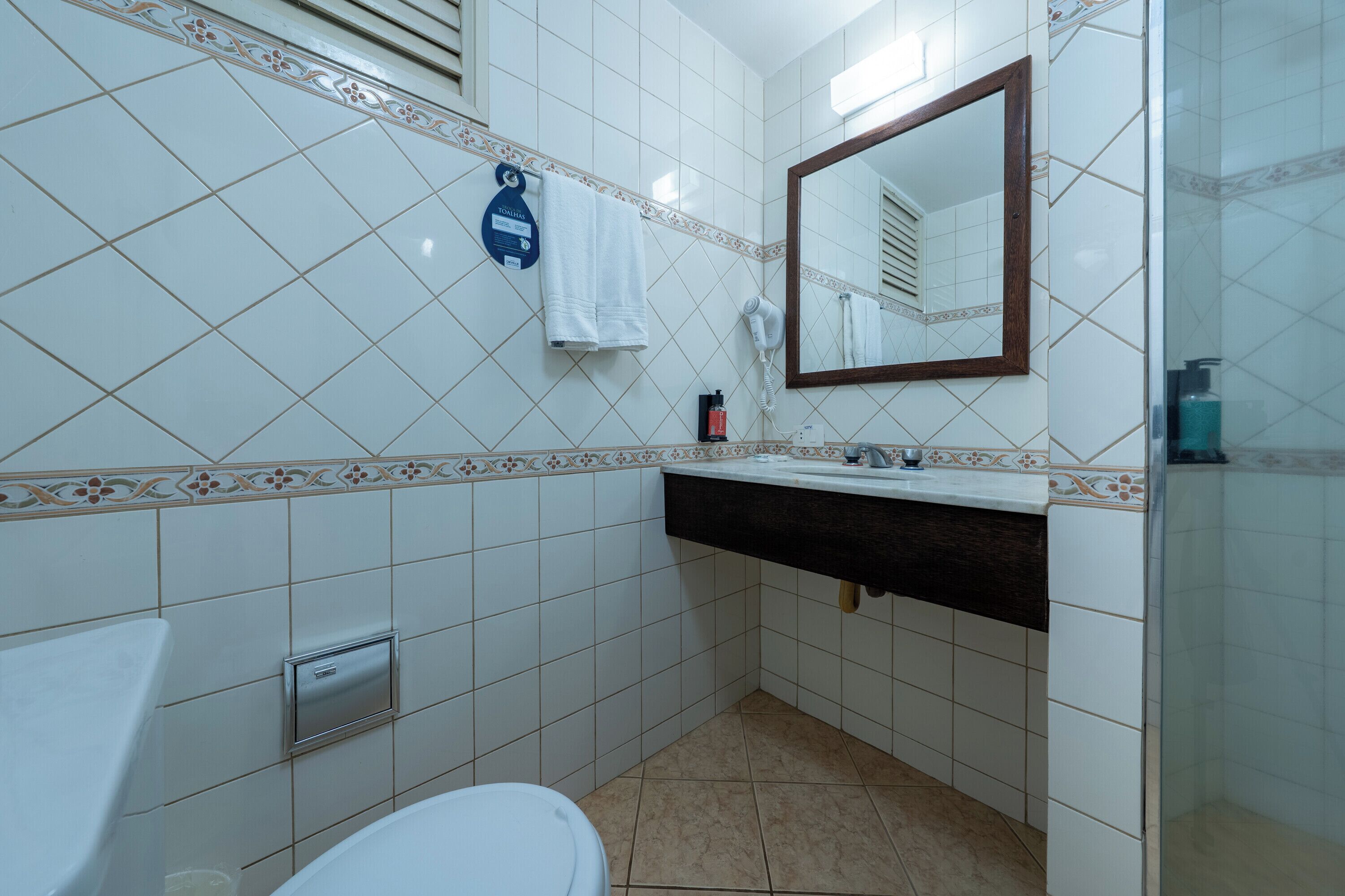 A bathroom with white tiles, a sink, a mirror, a towel rack, and a shower.