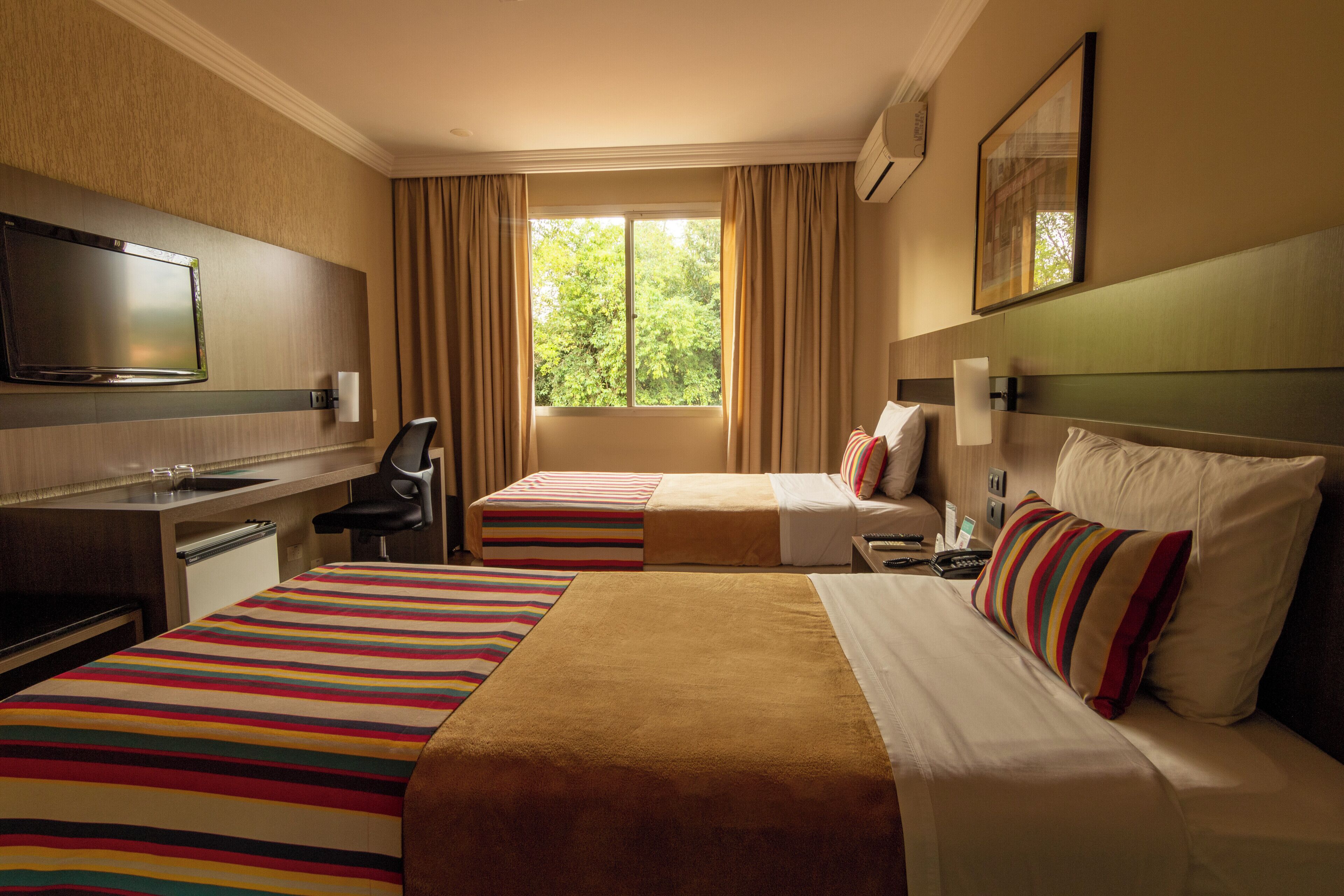 Une chambre d’hôtel avec deux lits, un bureau, une télévision et une fenêtre avec des rideaux.