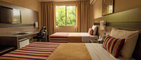 Habitación de hotel con dos camas, un escritorio, televisor y una ventana con cortinas.
