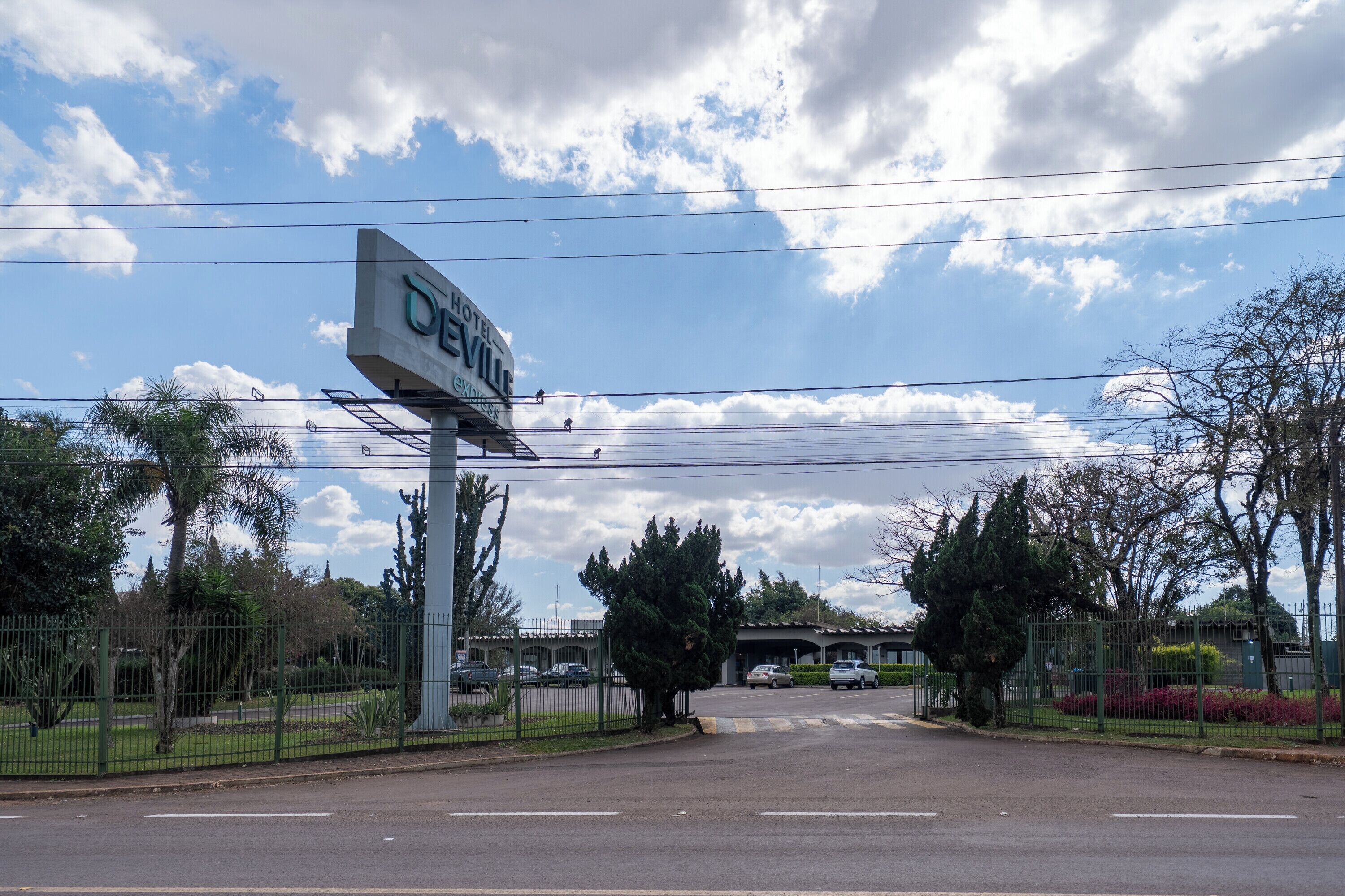 A hotel sign with a clear view of the entrance, surrounded by a fenced parking area and greenery.