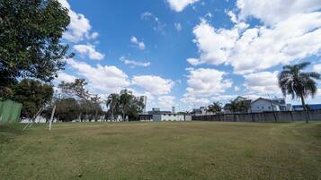 Un campo cubierto de césped con un arco de fútbol, árboles y edificios al fondo.